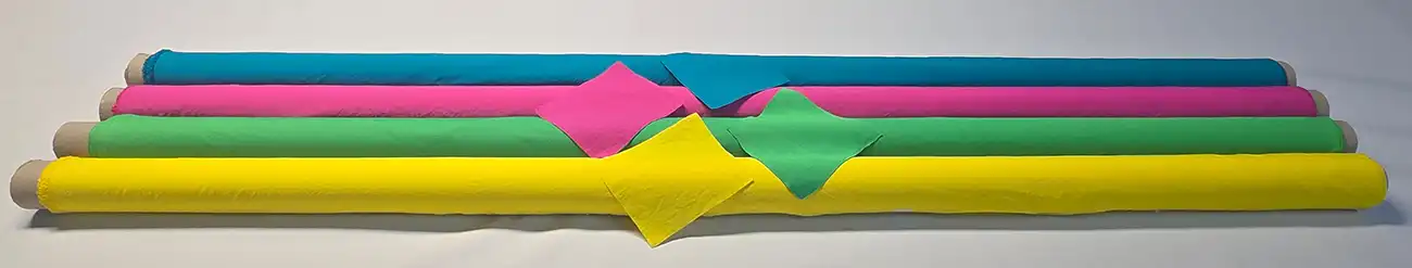 Four vibrant fabric rolls in blue, pink, green, and yellow with matching swatches displayed on a white background – Metro Dyeing mood board presentation.